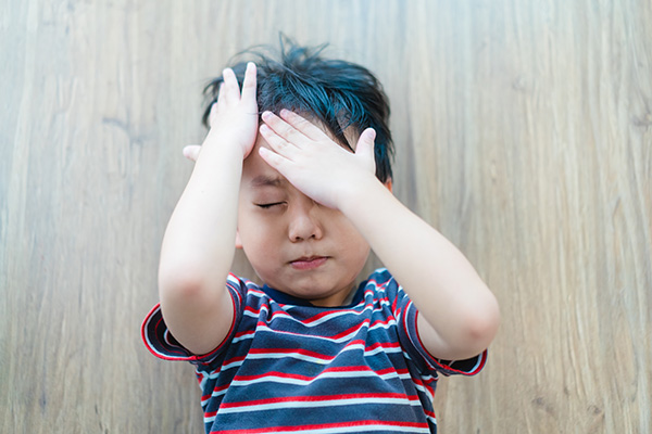 Little boy holds head and winces in pain