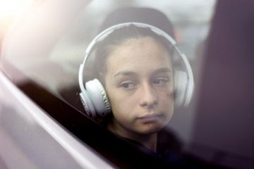 Sad girl wearing headphones staring out car window