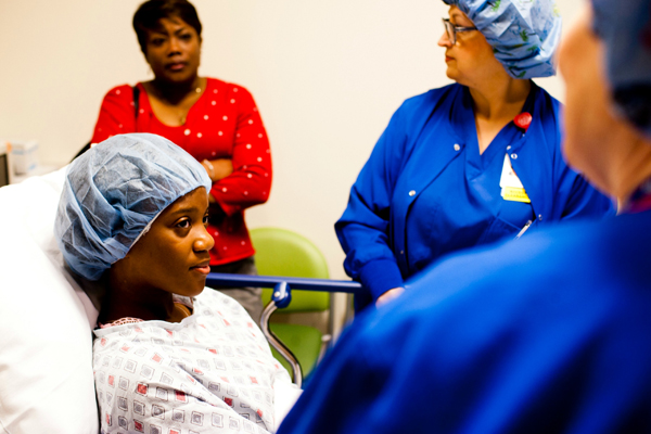 Nurses preparing teen girl for surgery with mom in the background